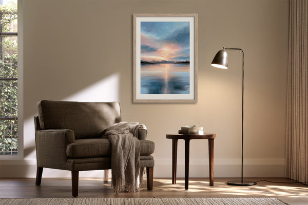 Light wood-framed mountain lake artwork above an upholstered armchair, side table, and floor lamp.