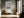 Light wood-framed mountain lake artwork above a small bench with an orange cushion in a hallway.