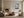 Light wood-framed mountain lake artwork above a low console near a fireplace and curved chair.