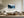 Framed winter pine forest artwork above a cream sectional sofa and wooden coffee table.