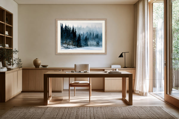 Framed snowy pine forest artwork above a wooden desk beside tall glass doors.