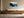 Framed winter pine forest artwork above a low wooden sideboard with ceramic vessels.