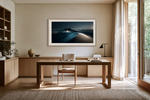 Light-framed dune artwork displayed above a wooden desk beside tall windows.