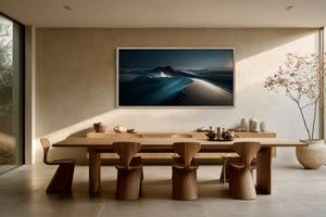Wide framed dune artwork above a long wooden dining table with sculptural chairs.