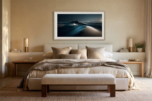 Light-framed dune artwork mounted above a bed with neutral layered bedding.