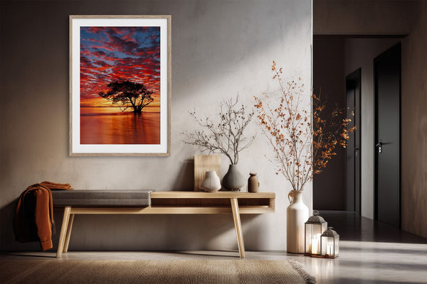 Light wood-framed sunset tree print above a wooden console with vases and dried branches.