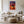 Light wood-framed sunset tree print above a white sofa, coffee table, and textured ottoman.