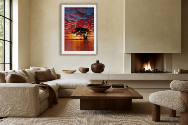 Light wood-framed sunset tree print above a sectional sofa near a lit fireplace.