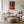 Light wood-framed sunset tree print above a white sofa, coffee table, and textured ottoman.