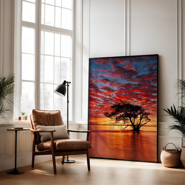 Large black-framed sunset tree artwork leaning against a wall beside an armchair.