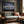 Large dark-framed snowy mountain reflection print above a gray sofa beside a wood-trimmed window.