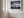 Light wood-framed mountain reflection print displayed on a white paneled wall beside tall windows.