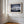 Light wood-framed mountain reflection print displayed on a white paneled wall beside tall windows.