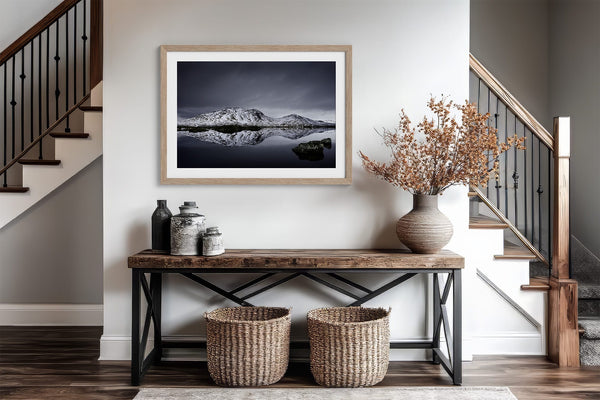 Light wood-framed mountain reflection print above a console table between two staircases.