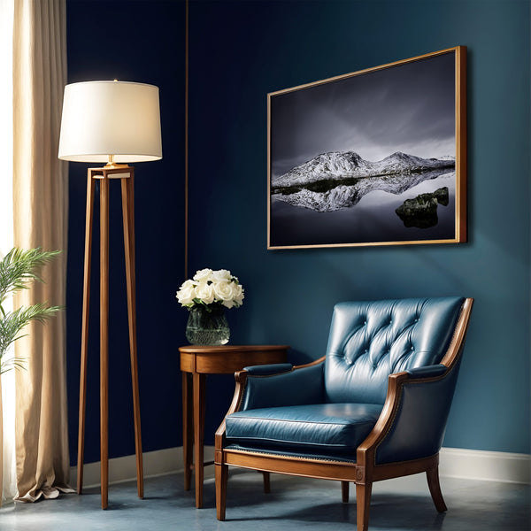 Thin dark-framed mountain reflection print on a deep blue wall above a blue leather armchair.