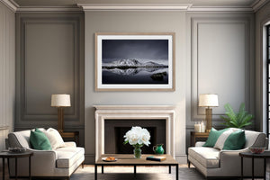 Light wood-framed mountain reflection print centered above a white fireplace between two armchairs.