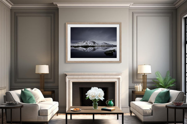 Light wood-framed mountain reflection print centered above a white fireplace between two armchairs.