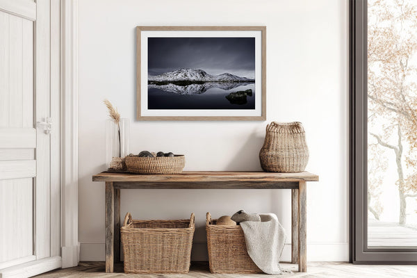 Light wood-framed mountain reflection print above a rustic console with woven baskets and pottery.