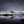 Snow-covered mountain ridge reflected in a still dark loch beneath a cloudy grey sky