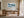 Framed snowy mountain artwork above a wooden desk near tall glass doors and curtains.