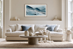Framed snowy mountain artwork above a white sofa with blue accent pillows and round coffee table.