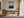 Light wood-framed mountain lake artwork above a wooden desk beside tall windows.