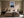 Light wood-framed mountain lake artwork centered above a beige upholstered bed.