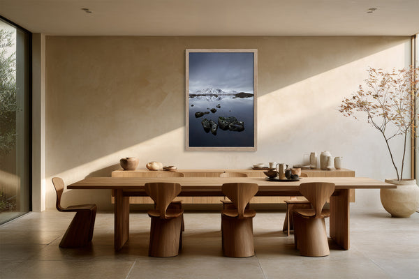 Light wood-framed mountain lake artwork above a long wooden dining table.