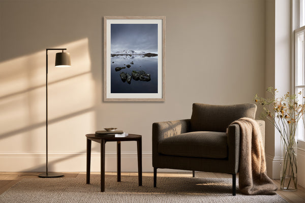 Light wood-framed mountain lake artwork above a dark armchair, side table, and floor lamp.