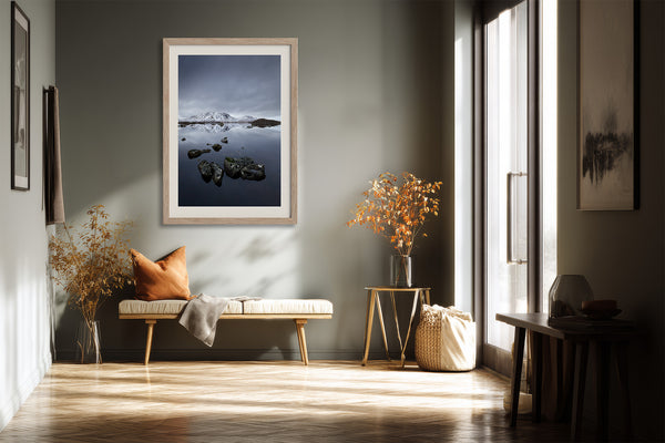 Light wood-framed mountain lake artwork above a bench with an orange cushion.