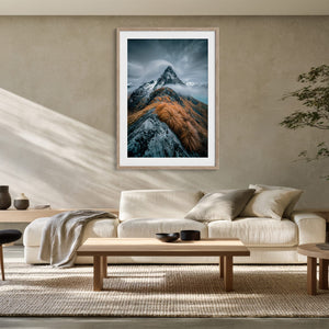 Framed mountain print above a cream sofa, low tables, and a potted indoor tree.