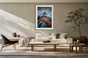 Framed mountain print above a cream sofa, low tables, and a potted indoor tree.