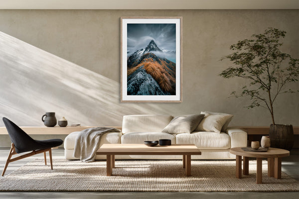 Framed mountain print above a cream sofa, low tables, and a potted indoor tree.