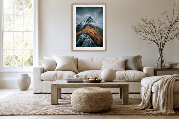 Framed mountain print above a cream sofa, coffee table, and woven ottoman.