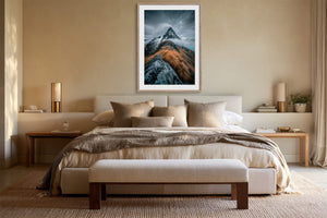 Framed mountain print centered above a bed with neutral bedding and bedside tables.