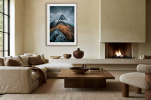 Framed mountain print above a sofa and coffee table beside a lit fireplace.