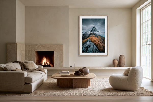 Framed mountain print over a low ledge in a living area with a lit fireplace.