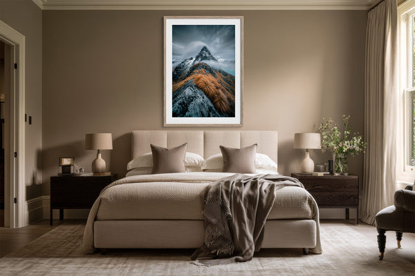 Framed mountain print above a bed with dark bedside tables and neutral bedding.