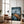 Large dark-framed mountain artwork leaning beside a brown armchair and floor lamp.