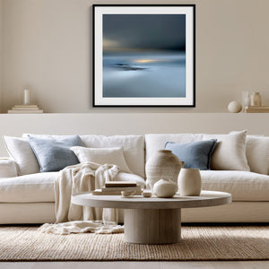 Black-framed Low Tide Light coastal print above a white sofa with pale blue cushions.