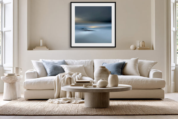 Black-framed Low Tide Light coastal print above a white sofa with pale blue cushions.