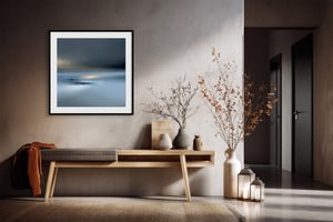 Black-framed Low Tide Light coastal print above a wooden console with dried branches and lanterns.