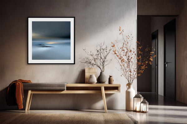 Black-framed Low Tide Light coastal print above a wooden console with dried branches and lanterns.