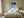 Black-framed Low Tide Light coastal print centered above a bed with white bedding and wood nightstands.