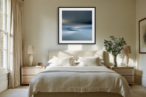 Black-framed Low Tide Light coastal print centered above a bed with white bedding and wood nightstands.