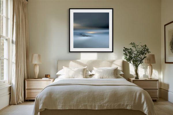 Black-framed Low Tide Light coastal print centered above a bed with white bedding and wood nightstands.