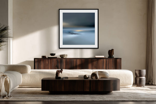 Black-framed Low Tide Light coastal print above a dark wood sideboard behind a curved cream sofa.