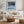 Black-framed Low Tide Light coastal print above a white sofa, wood coffee table, and woven ottoman.