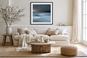 Black-framed Low Tide Light coastal print above a white sofa, wood coffee table, and woven ottoman.