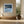 Black-framed Low Tide Light coastal print above a built-in bench beside large black-framed windows.